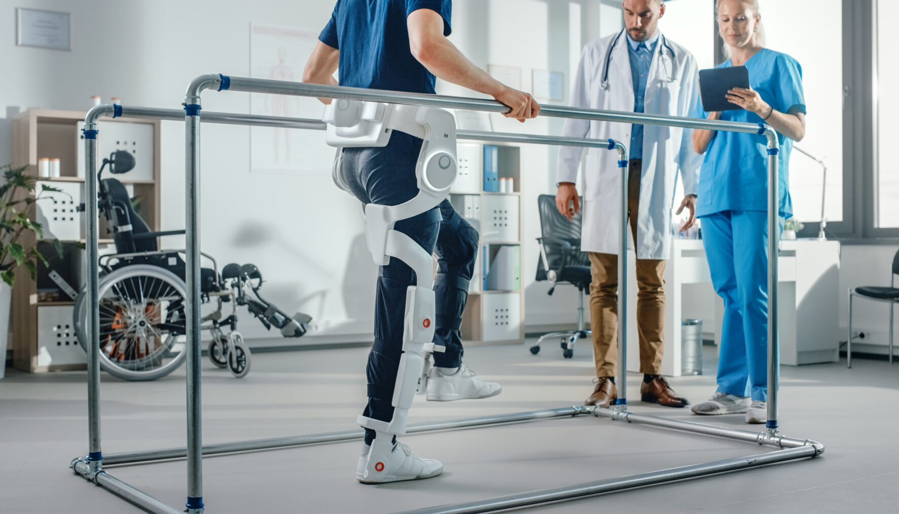 Modern Hospital Physical Therapy: Patient with Injury Walks Wearing Advanced Robotic Exoskeleton. Physiotherapy Rehabilitation Scientists, Engineers use Tablet Computer to Help Disabled Person